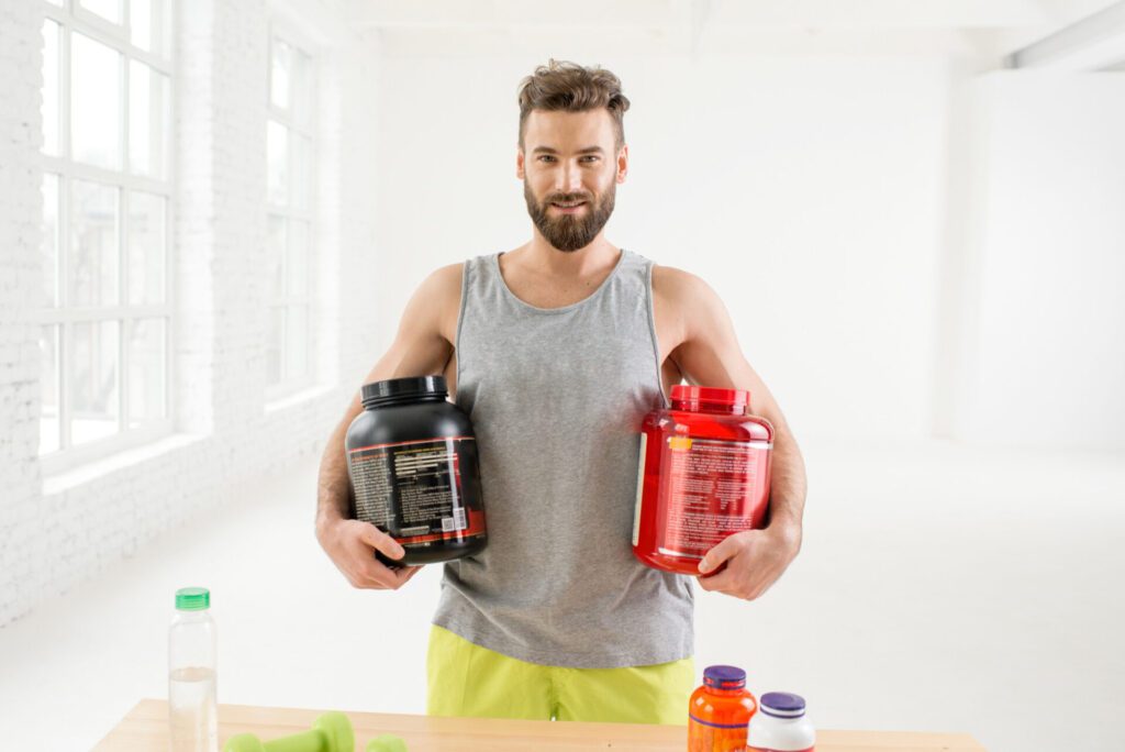 athletic-man-holding-bottles-with-sports-nutriton-white-gym-interior