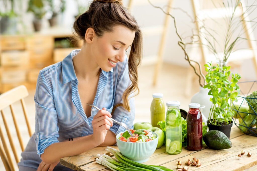 young-happy-woman-eating-healthy-salad-sitting-table-with-green-fresh-ingredients-indoors