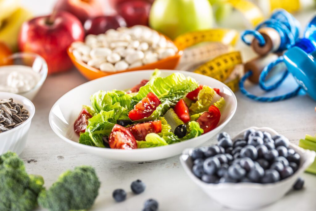 Healthy fresh salad with tomatoes olives and olive oil, surrounded by healthy food and exercise equipment.