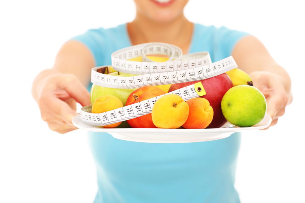 Midsection of a woman holding fruits and tape measure