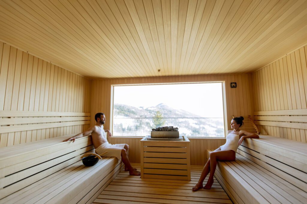 Young couple relaxing in the sauna and watching winter forest th