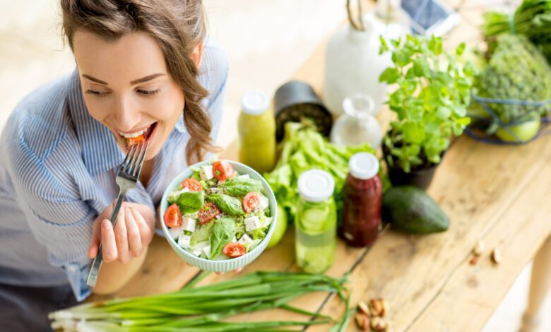 young happy woman eating healthy salad sitting table with green fresh ingredients indoors