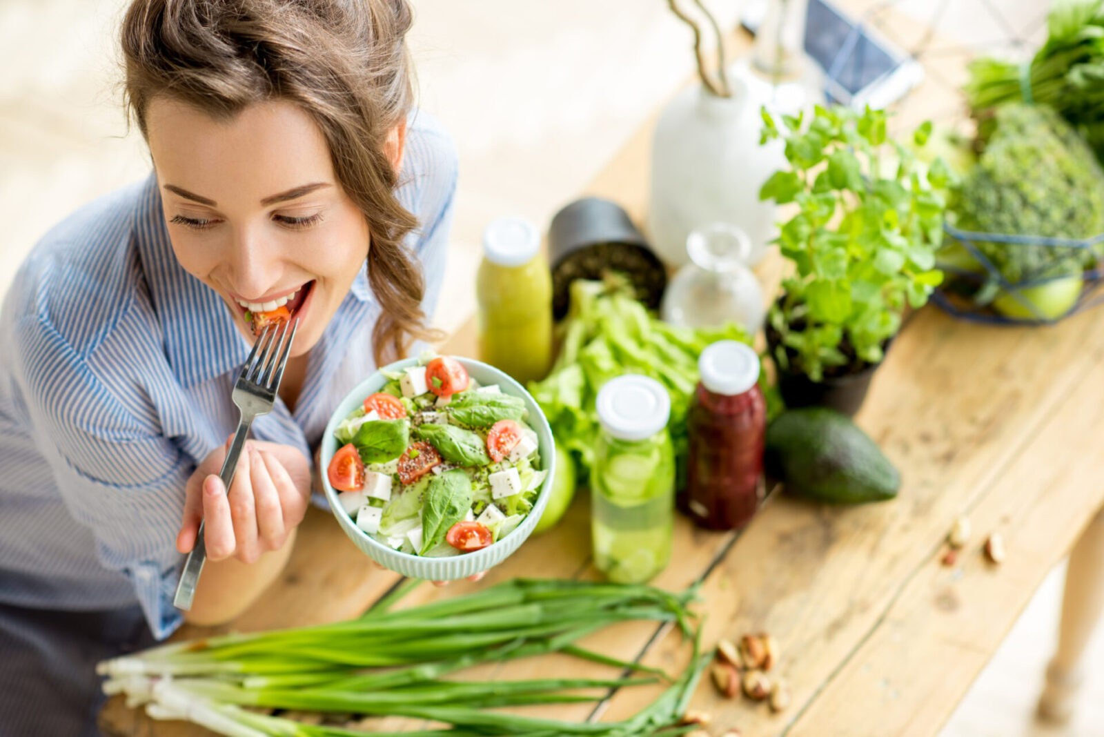 young happy woman eating healthy salad sitting table with green fresh ingredients indoors