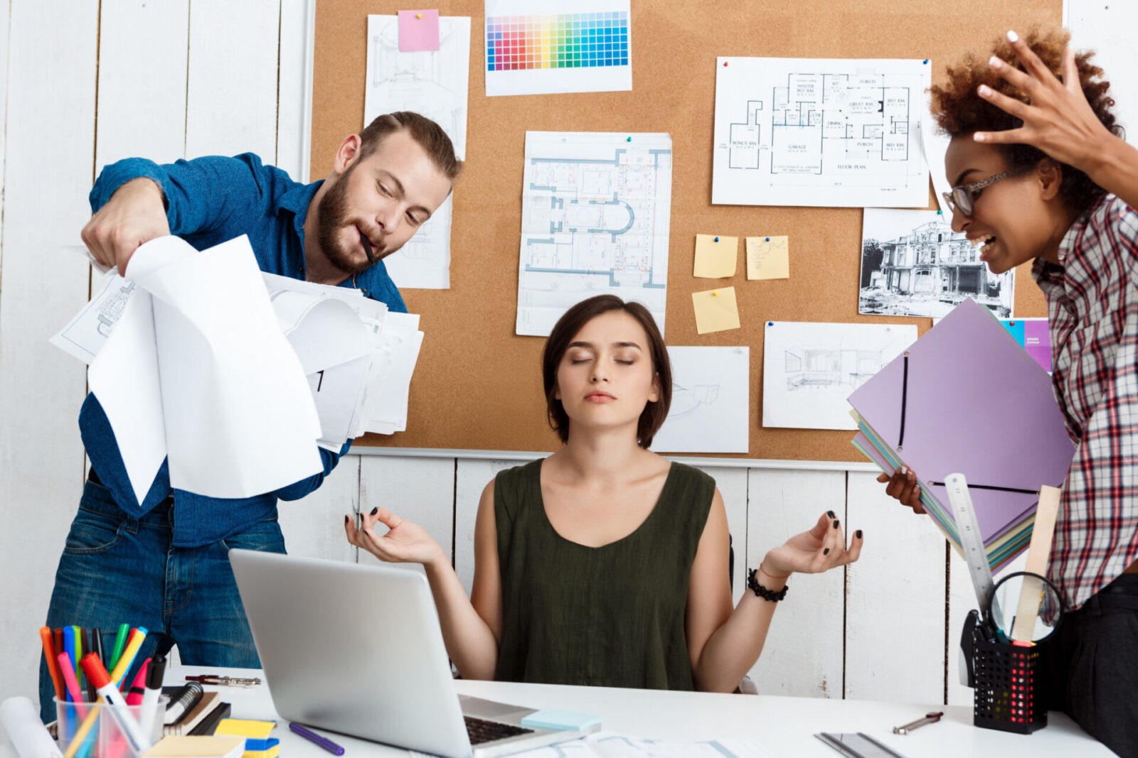 Colleagues debating over drawings while a woman practices meditation for stress relief in the workplace