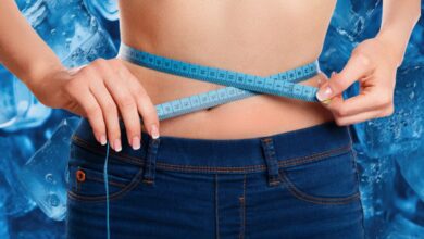 Ice cubes in focus with blurred background of a person measuring waist, illustrating the concept of Ice Hack for weight loss.