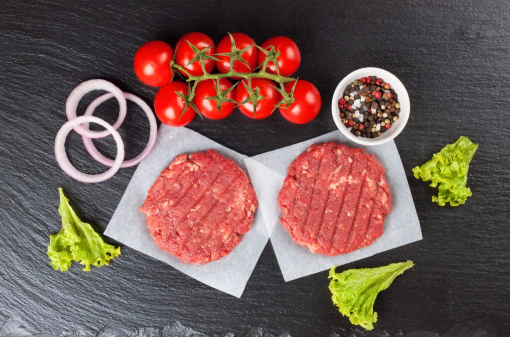 fresh raw home made minced beef steak burger with spices tomatoes salad black slate table top view flat lay