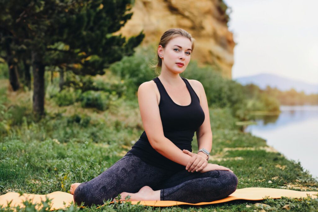 girl black sportswear does stretch by river while sitting mat